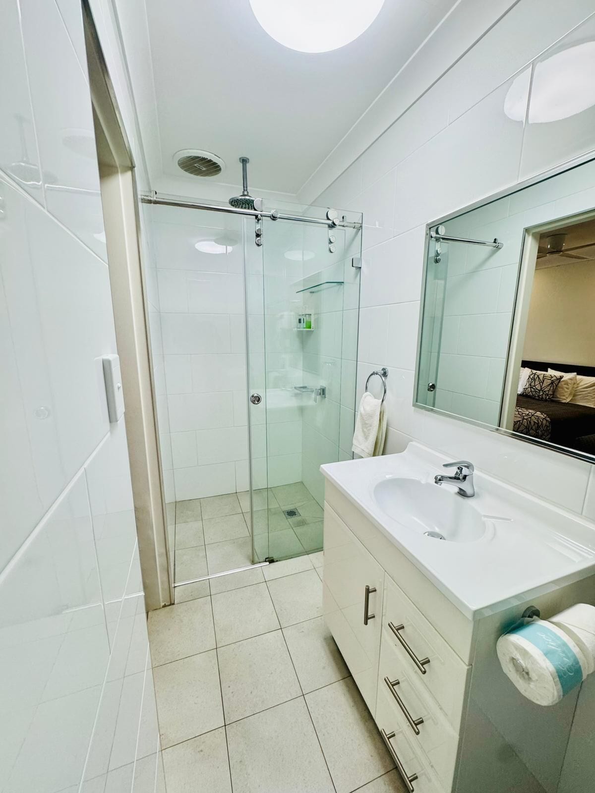 Un baño moderno con ducha de vidrio, lavamanos blanco con espejo y un inodoro.