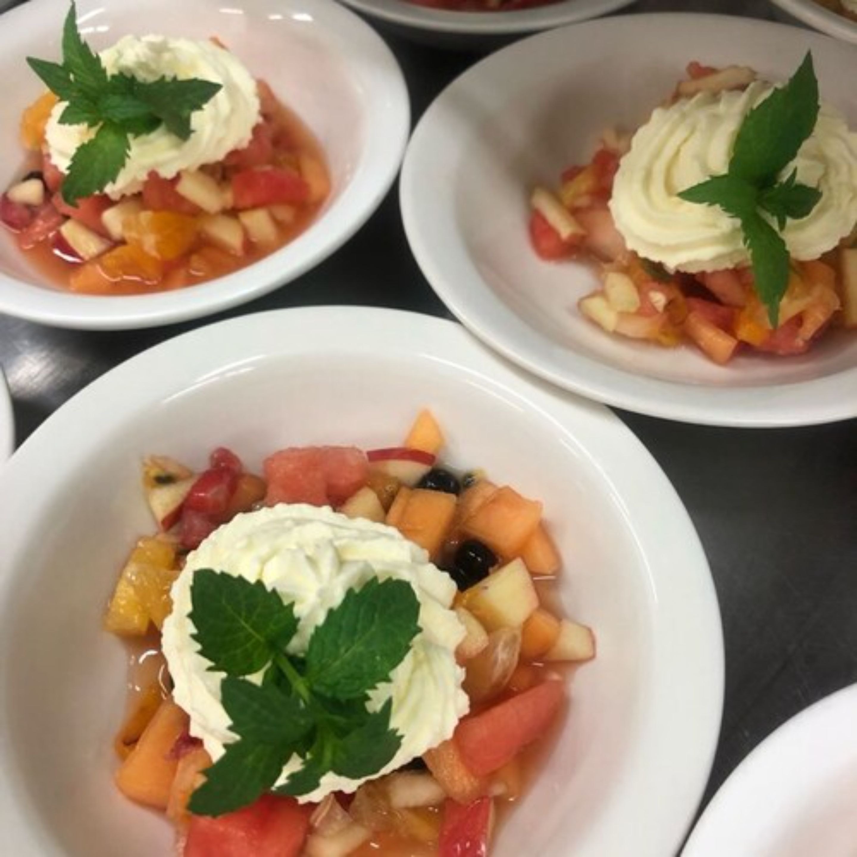 Trois bols de salade de fruits, garnis de crème fouettée et de feuilles de menthe.