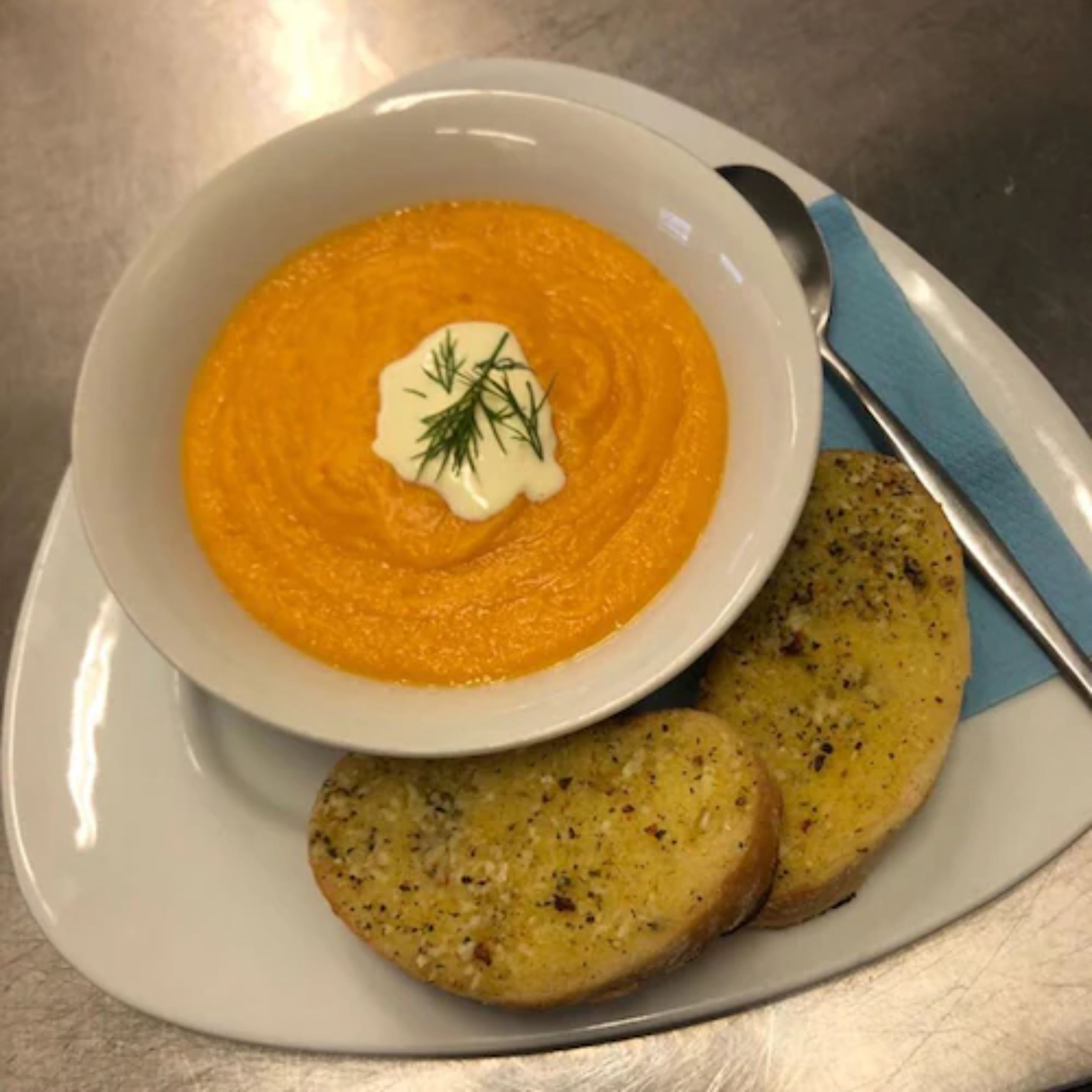 A bowl of creamy orange soup garnished with dill, accompanied by two slices of garlic bread on a white plate.