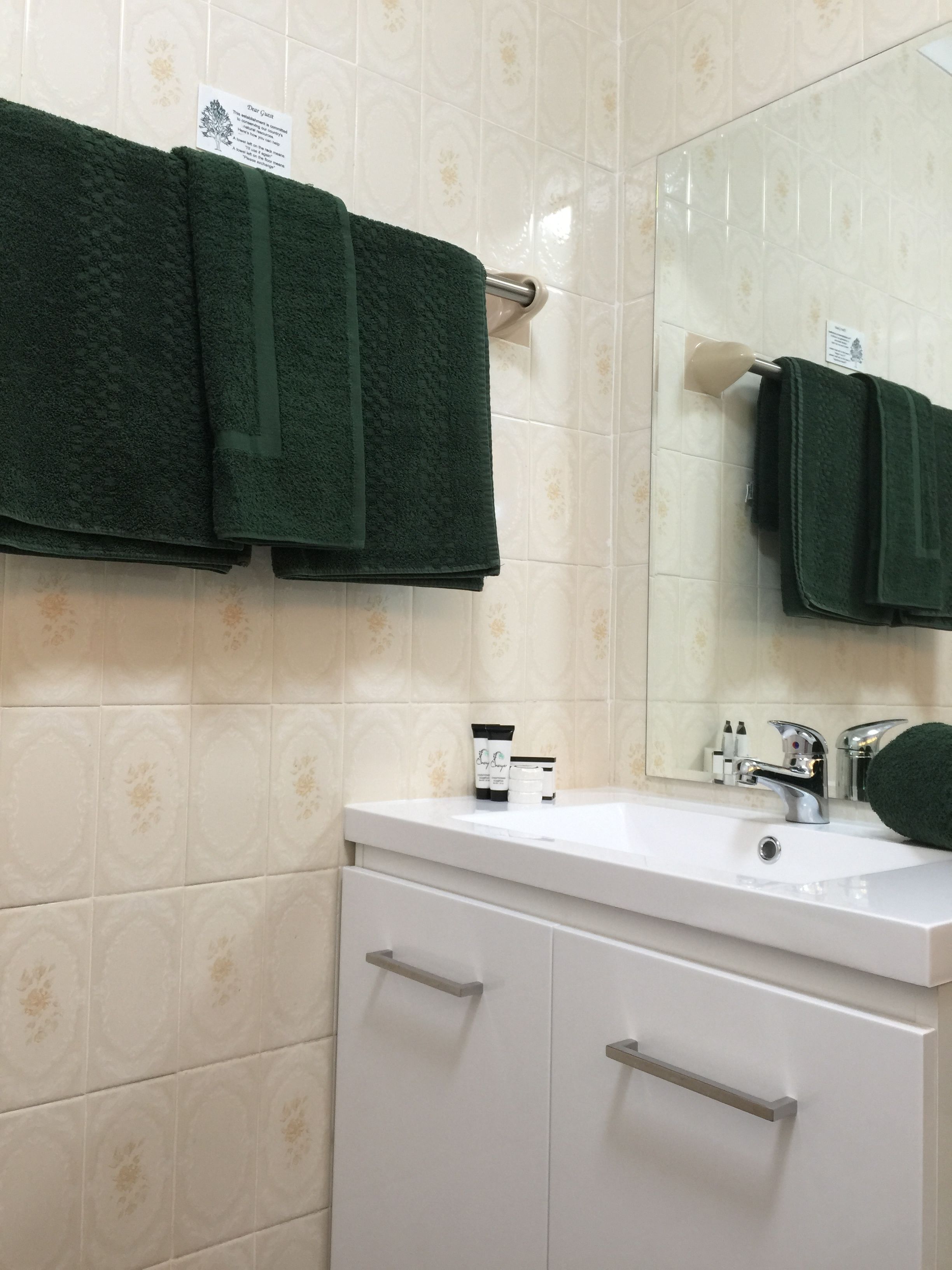 A bathroom with a white vanity, two drawers, a mirror, and a towel rack with two green towels.