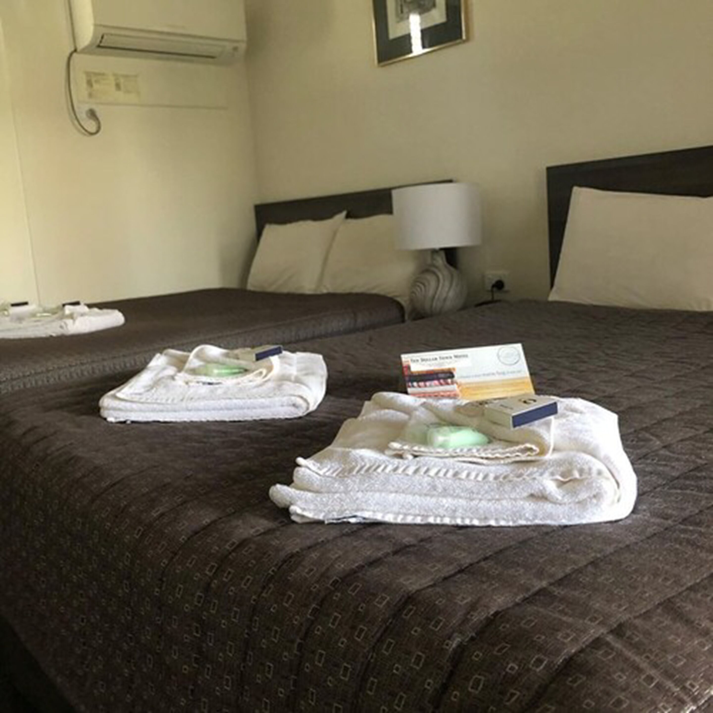 A neatly made bed with a brown patterned bedspread, two folded white towels, and a small stack of books on the bed.