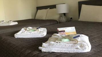A neatly made bed with a brown patterned bedspread, two folded white towels, and a small stack of books on the bed.