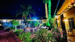 Un patio al aire libre con mesas y sillas, una palmera y un edificio con luces colgantes.
