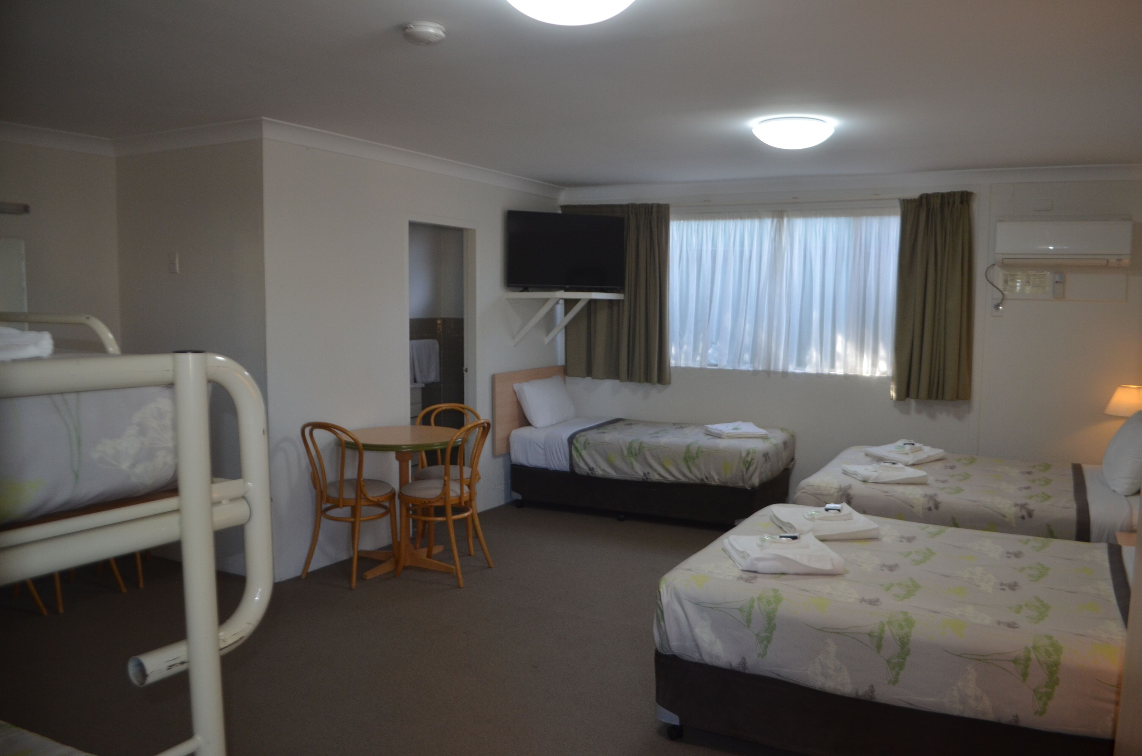 A hotel room with two beds, a TV, a small table with chairs, and a window with curtains.