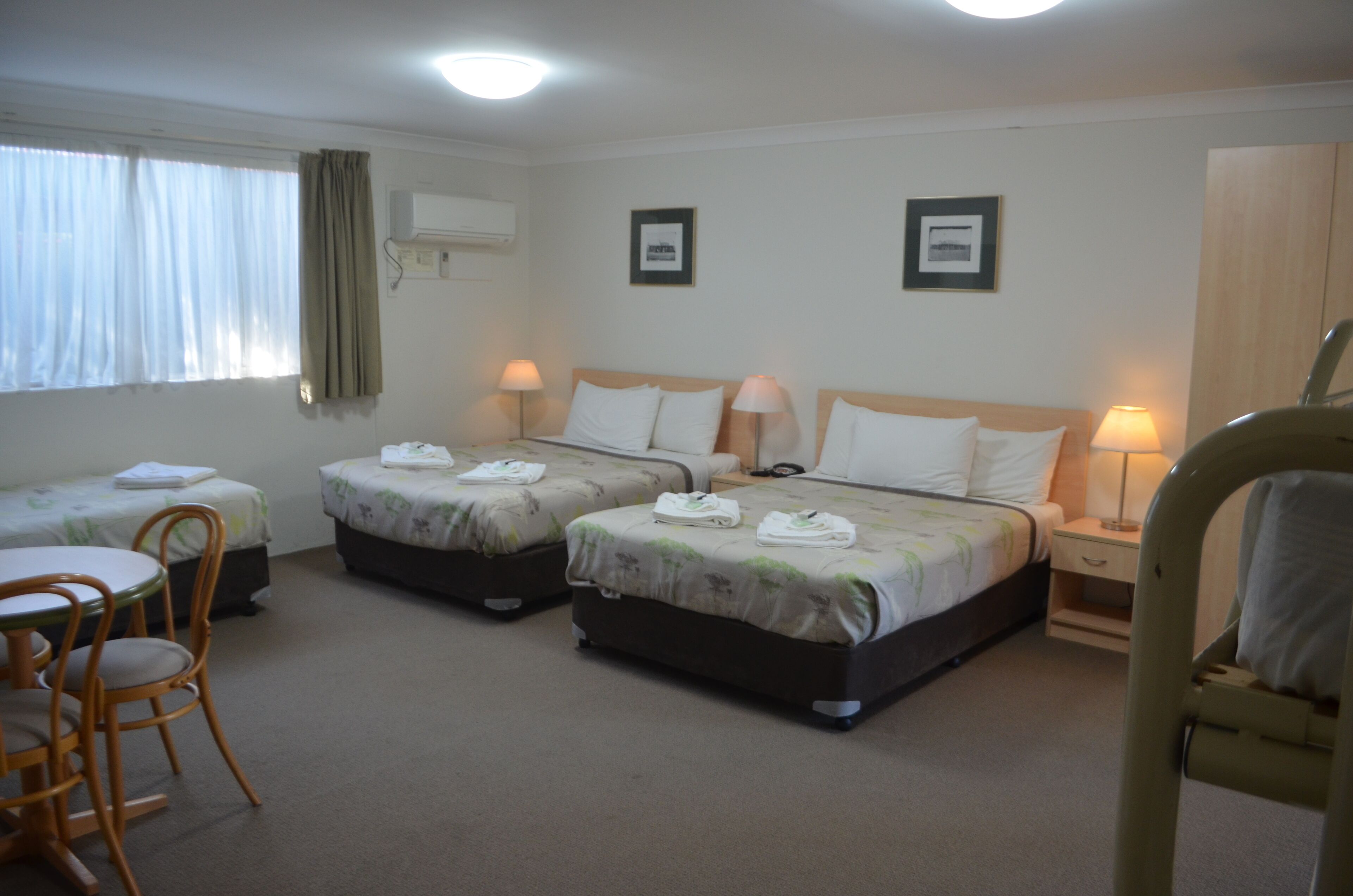 A hotel room with three single beds, a small table with chairs, and a desk with a chair.