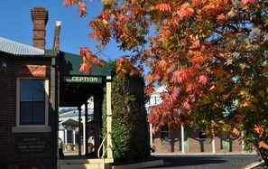 A reception area with a sign, a brick building, and a tree with autumn leaves. - Ten Dollar Town Motel (Gulgong)
