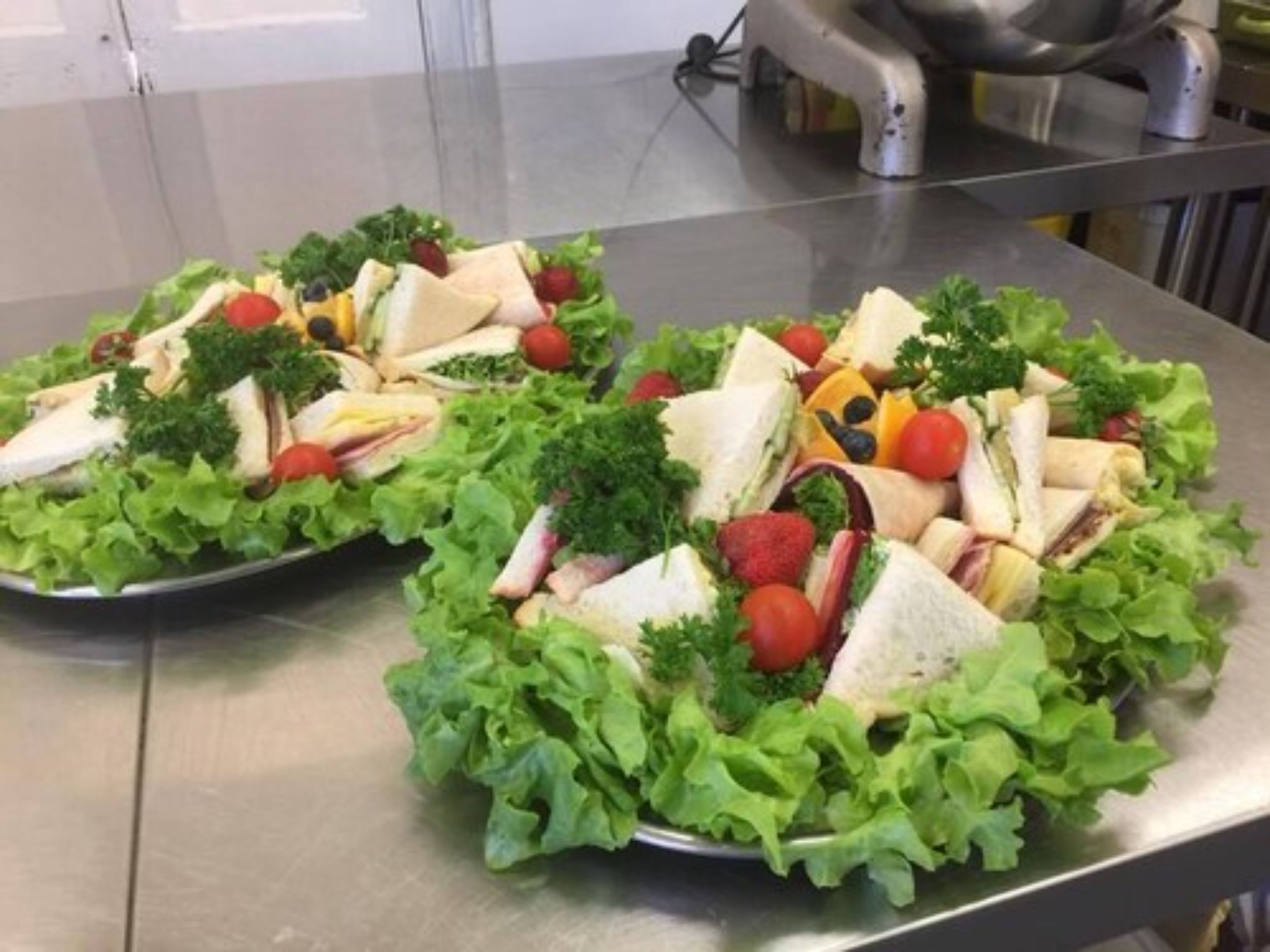 A stainless steel table with two trays of sandwiches and salad.