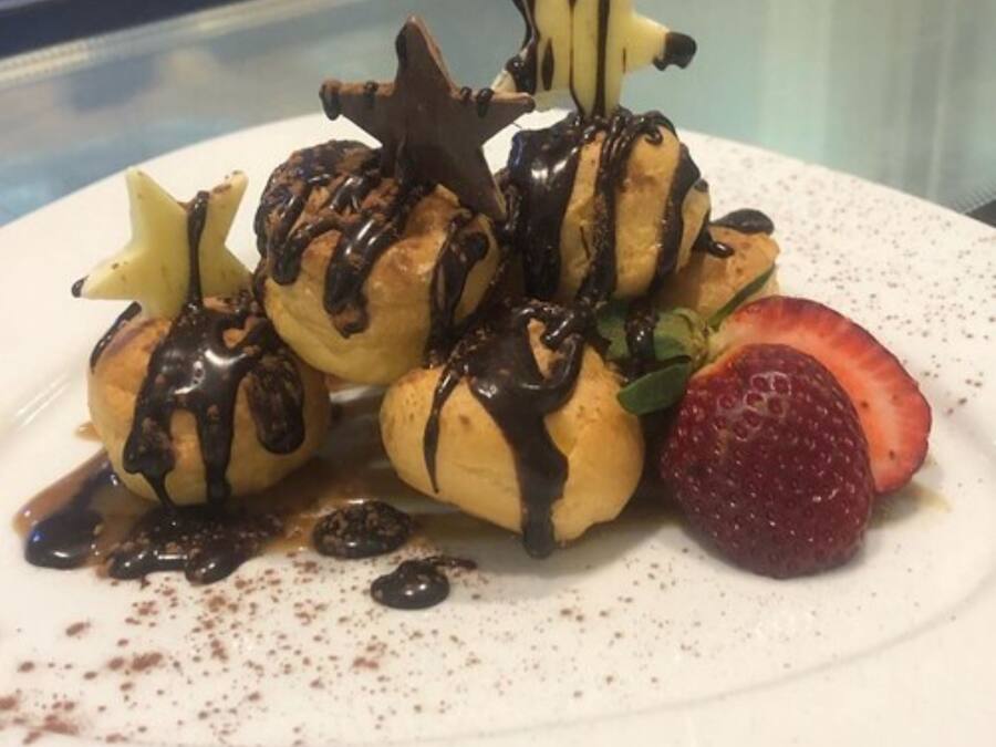 Een nagerechtenbord met éclairs, chocoladesiroop en een aardbei.