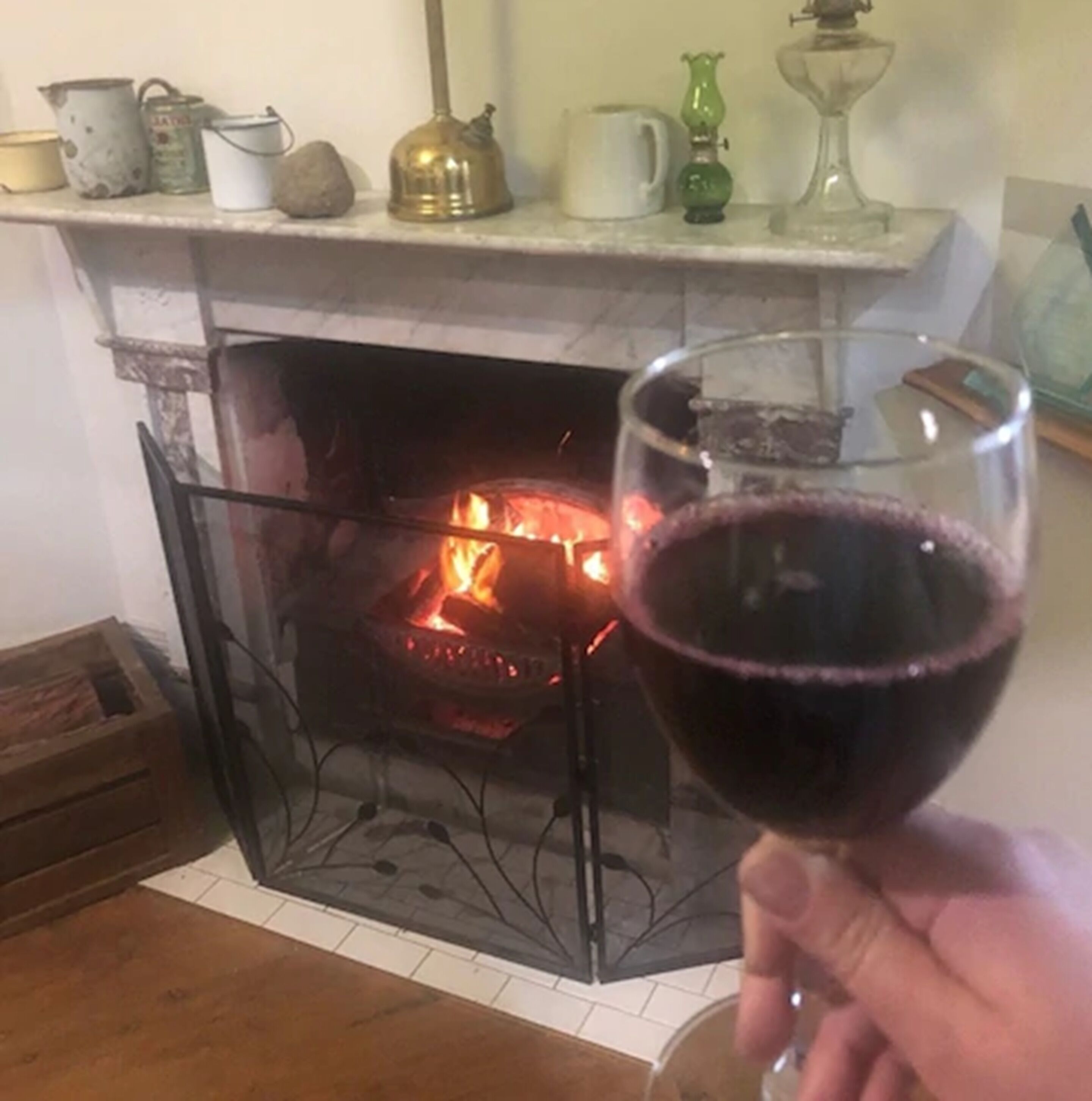 A fireplace with a visible fire, a glass of red wine, and various items on the mantel.