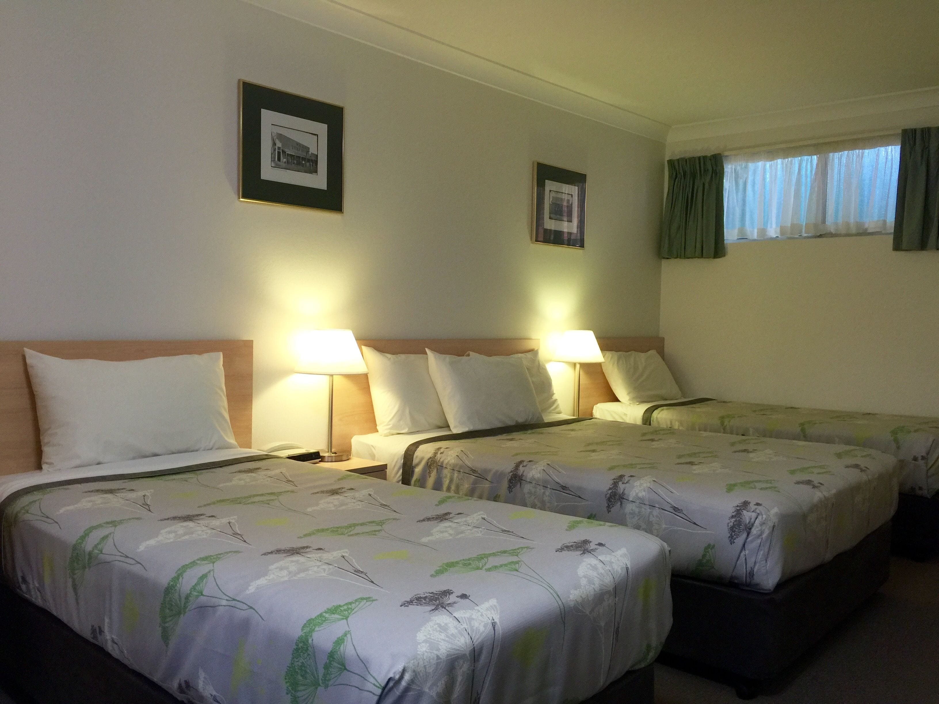 Habitación de hotel con dos camas, cada una con cubrecama floral, lámparas de noche y cuadros en la pared.