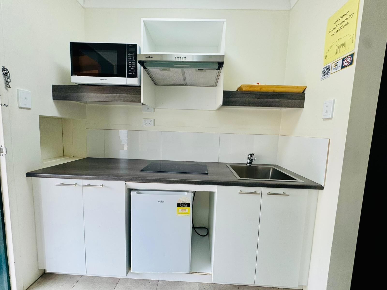 A compact kitchen with a microwave, a built-in oven, a sink, and a small refrigerator.
