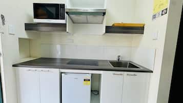 A compact kitchen with a microwave, a built-in oven, a sink, and a small refrigerator.