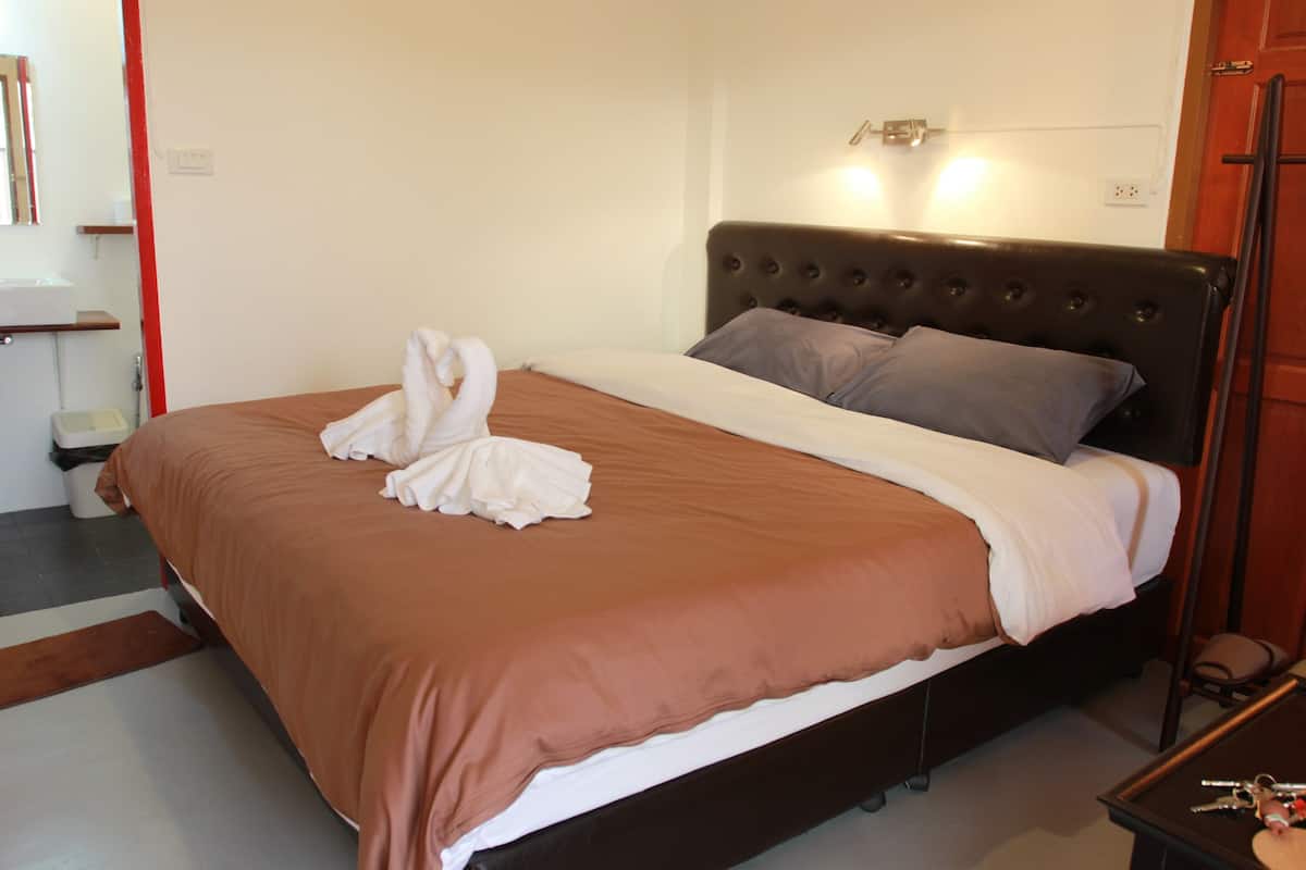 A neatly made bed with a brown bedspread and white pillows, a bedside table with a lamp, and a wooden floor.