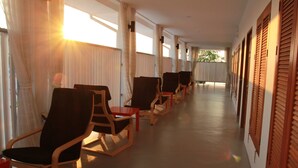 A corridor with wooden rocking chairs and a wooden floor, leading to a door with a window. - Barefeet Naturist Resort (Bangkok)
