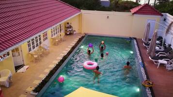 An indoor swimming pool with a tiled roof, surrounded by lounge chairs and a small deck area.