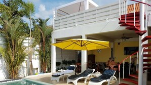 A pool area with lounge chairs and a yellow umbrella, surrounded by tropical plants. - Barefeet Naturist Resort (Bangkok)