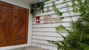 A wooden double door with intricate carvings, a white wall with horizontal siding, and a sign reading "Baan Barefeet". - Barefeet Naturist Resort (Bangkok)