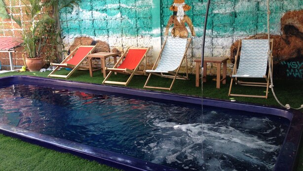 A swimming pool with four lounge chairs, a potted plant, and a mural on the wall. - Barefeet Naturist Resort (Bangkok)