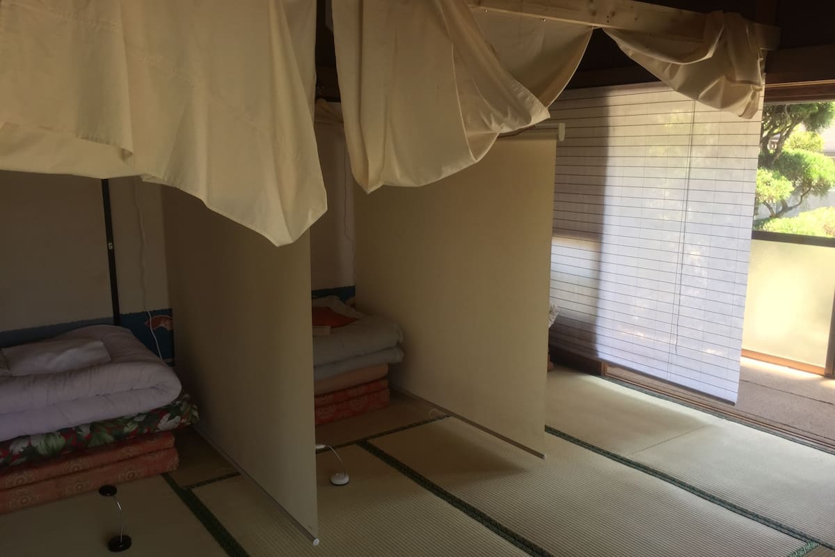 Une pièce de style japonais traditionnel, avec un sol recouvert de tatamis, un lit bas doté d’un baldaquin et une porte coulissante en papier de riz (shoji).