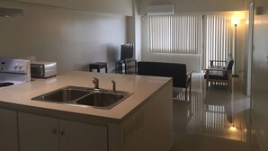 A modern kitchen with a central island, a ceiling fan, and a dining area with a table and chairs. - Pia Marine Condominium (Tamuning)