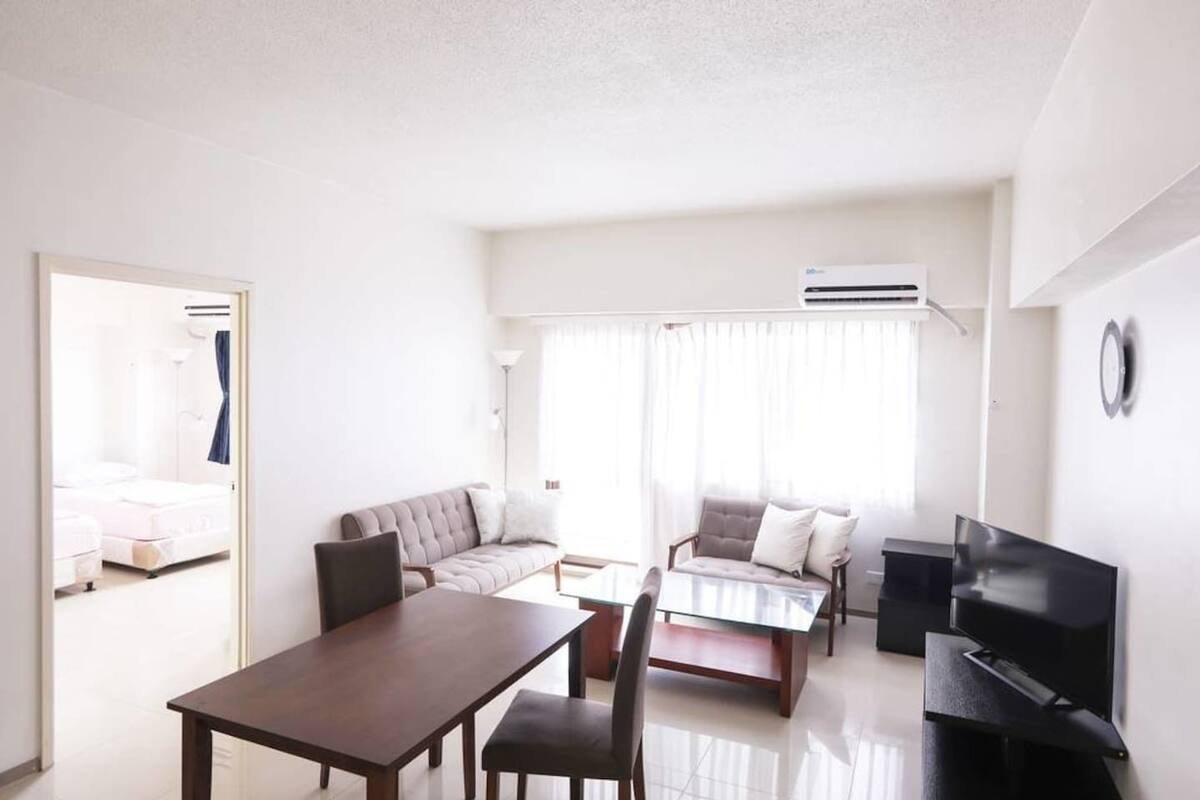 A modern hotel room with a dining table, sofa, and TV.