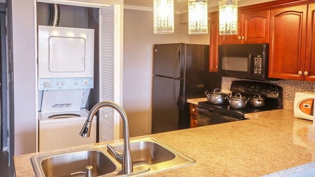 A kitchen with a double sink, stainless steel appliances, wooden cabinets, and pendant lighting. - Pia Marine Condominium (Tamuning)