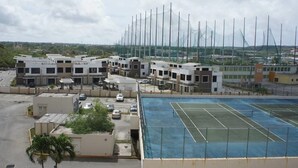 A tennis court with a net, surrounded by buildings and a parking lot. - Pia Marine Condominium (Tamuning)