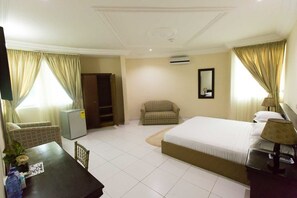 A hotel room with a bed, a chair, a desk, a wardrobe, and a TV. - Karela Beach Resort (Beyin)