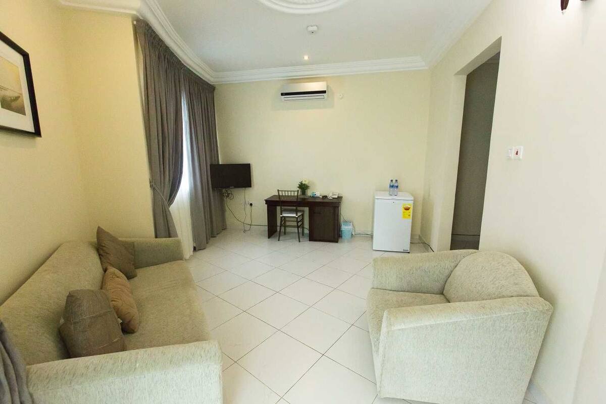 A living room with two sofas, a TV, a desk, and a refrigerator.