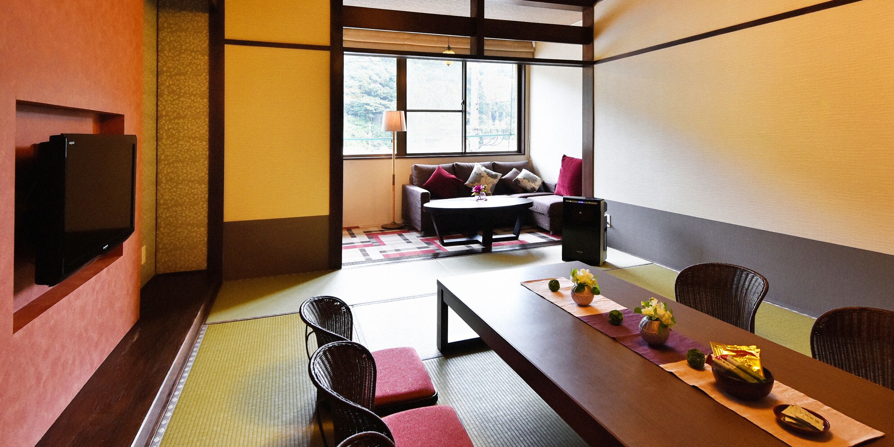 A traditional Japanese-style room with tatami flooring, a low table with cushions, and a television on the wall.