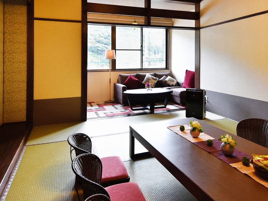A traditional Japanese-style room with tatami flooring, a low table with cushions, and a television on the wall.