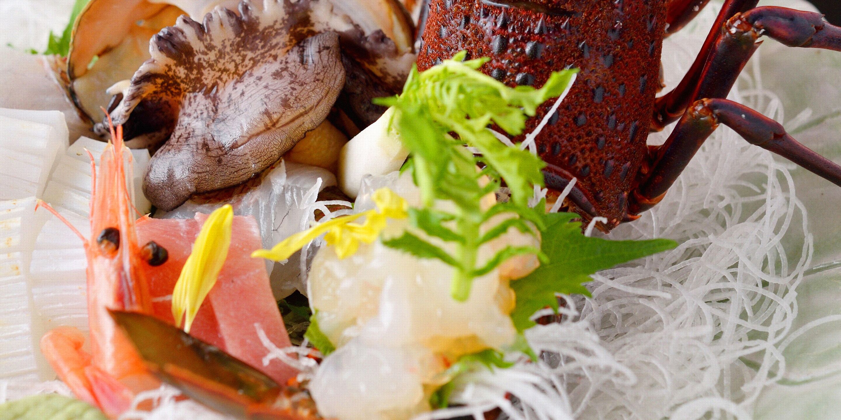A variety of seafood including shrimp, scallops, and a lobster tail, served on a bed of shredded white material, possibly rice paper.