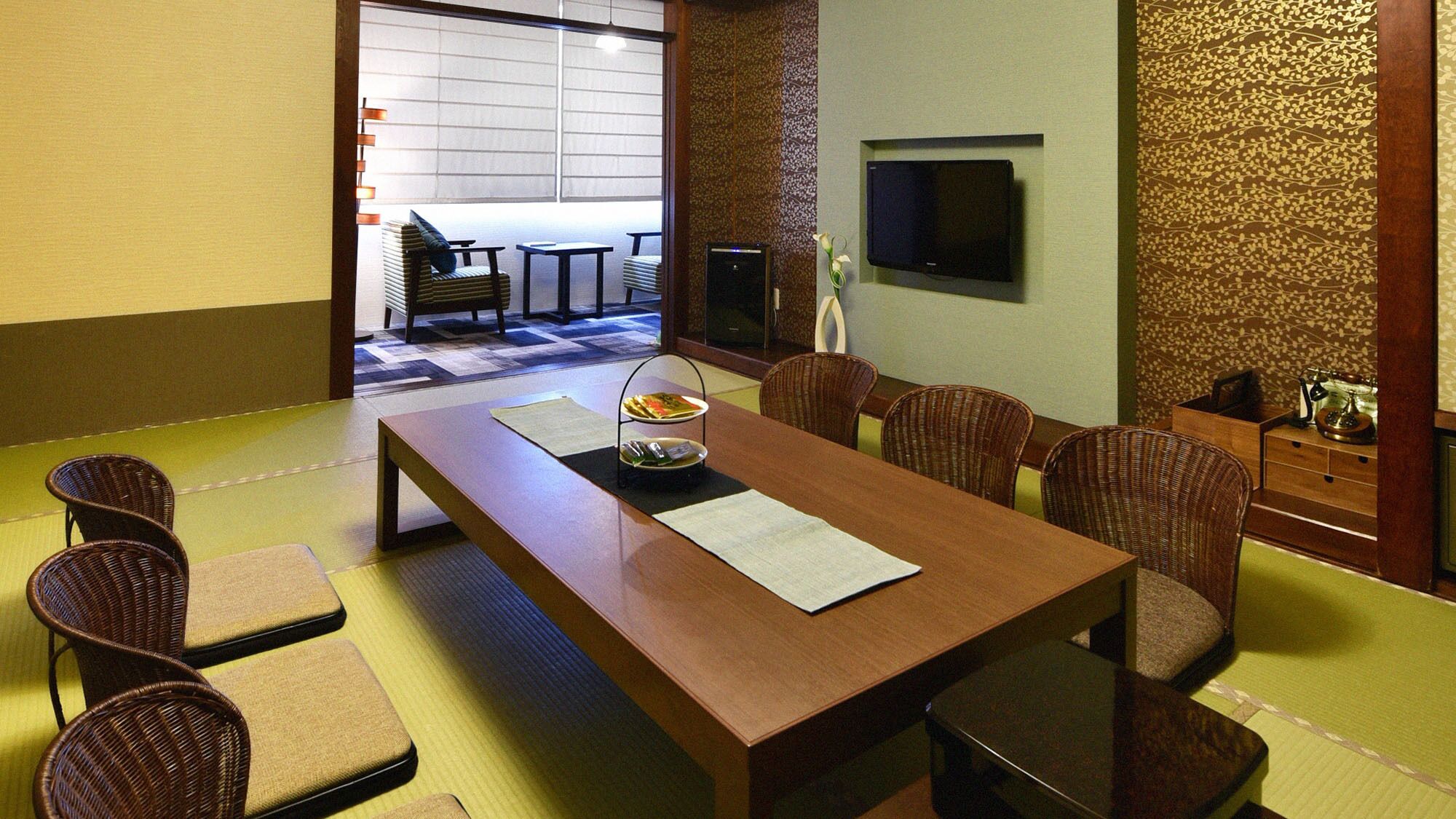Una habitación tradicional japonesa con suelo de tatami, una mesa baja con cojines y un televisor montado en la pared.