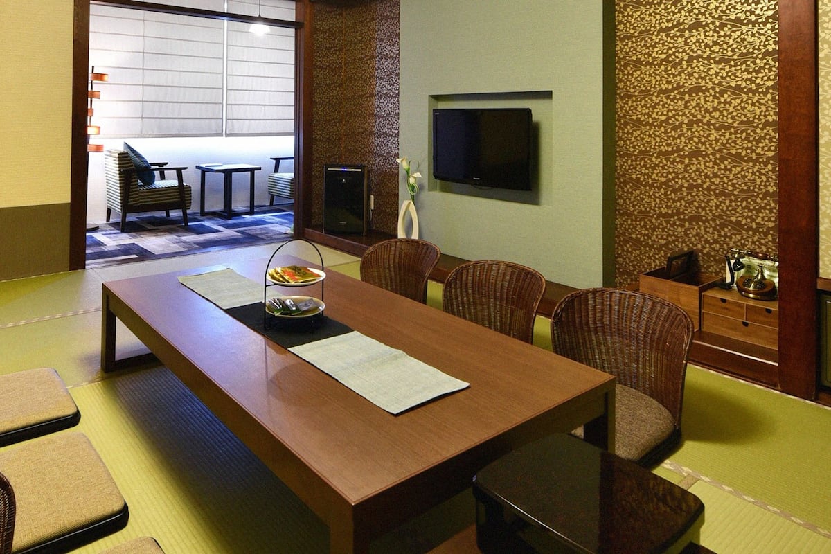 A traditional Japanese-style room with tatami flooring, a low table with cushions, and a television mounted on the wall.