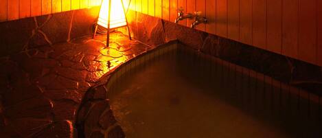 A stone-floored hot tub area with a wooden wall and a wall-mounted light fixture.