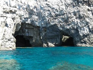 A rocky cliff with two caves at the base, overlooking clear blue water. - Hotel Avan Sukumo (Sukumo)