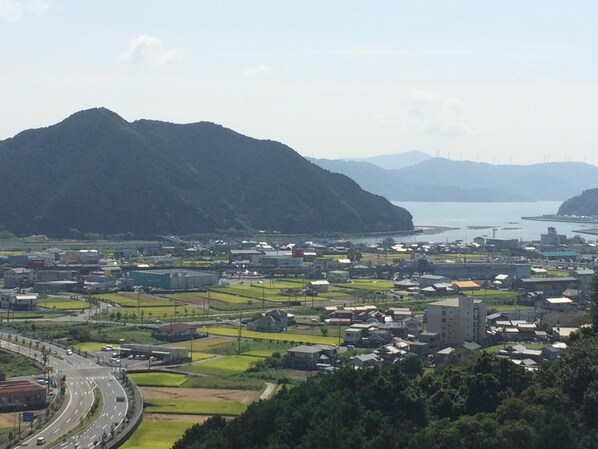 A coastal town with a mix of residential and industrial buildings, a highway, and mountains in the background. - Hotel Avan Sukumo (Sukumo)