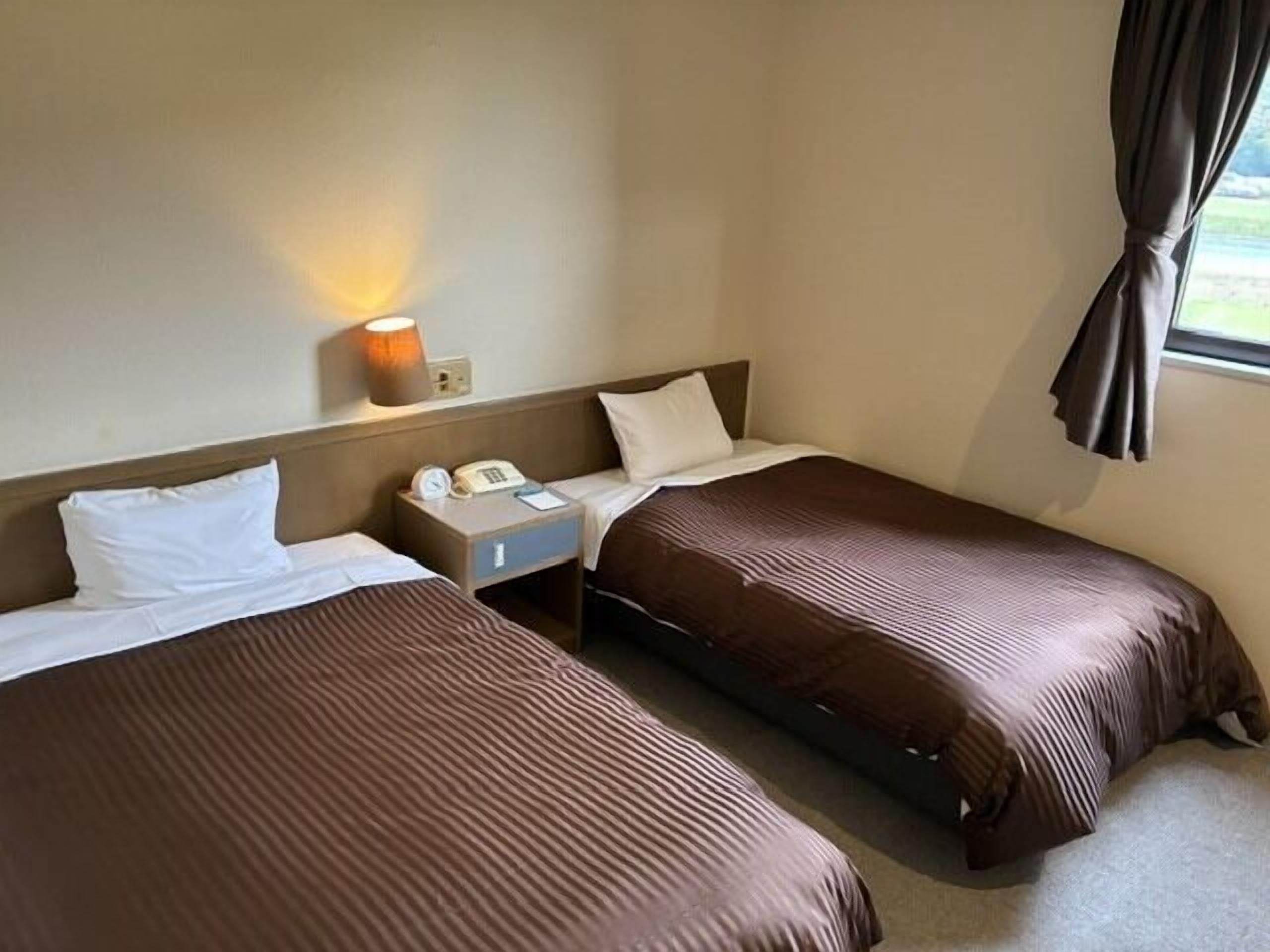 Une chambre d’hôtel avec deux lits, une table de chevet avec une lampe, un téléphone et une fenêtre avec des rideaux.