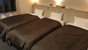 Habitación de hotel con tres camas individuales, cada una con cubrecama marrón y almohadas blancas. Dos lámparas de pared proporcionan luz.