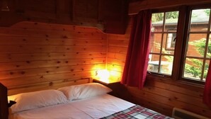 A wooden cabin room with a bed, a nightstand, a window with a view of the outdoors, and a red curtain. - Lurchers Cabin Aviemore (Aviemore)