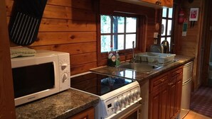 A compact kitchen with wooden cabinets, a microwave, a stove, and a sink. - Lurchers Cabin Aviemore (Aviemore)