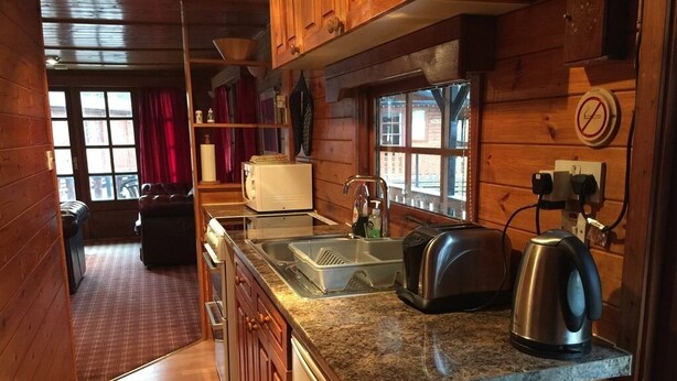 A compact kitchen with wooden cabinets, a granite countertop, a sink, a toaster, and a kettle. - Lurchers Cabin Aviemore (Aviemore)