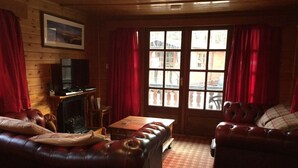 A cozy living room with leather sofas, a fireplace, and a large window with curtains. - Lurchers Cabin Aviemore (Aviemore)