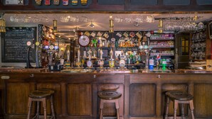 Una zona de bar con taburetes de madera, una variedad de botellas y un menú en una pizarra.