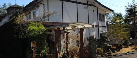 A traditional Japanese house with a covered entrance, a wooden gate, and a signboard.