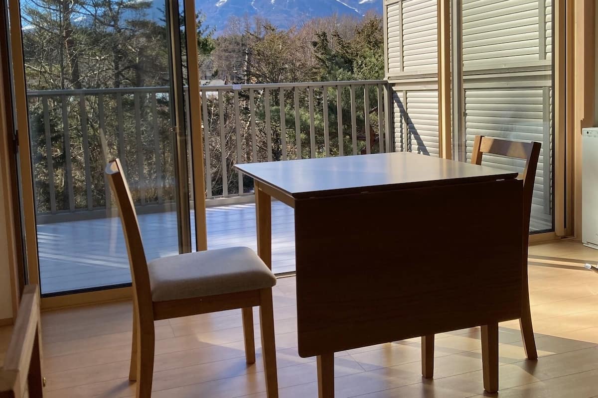 A room with a wooden table and chairs, large sliding glass doors, and a view of a snow-capped mountain.