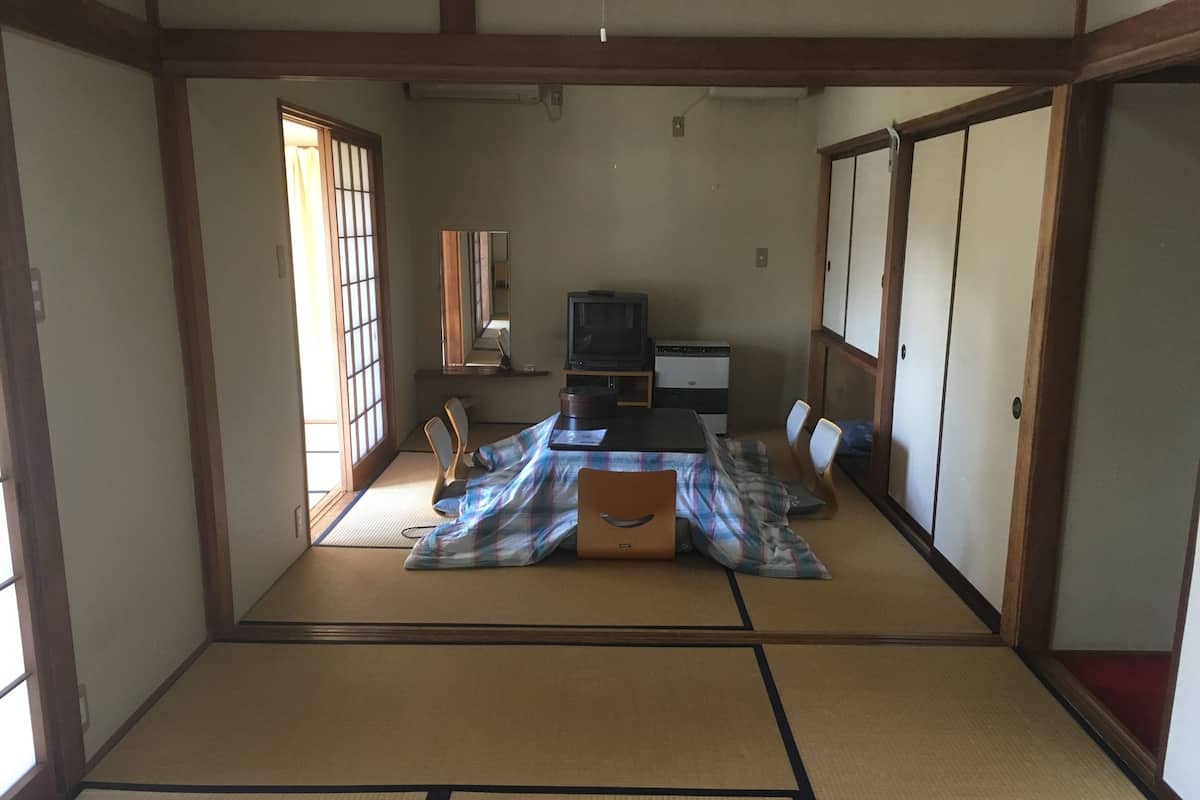 A traditional Japanese room with tatami flooring, a low table with cushions, a television, and sliding doors.