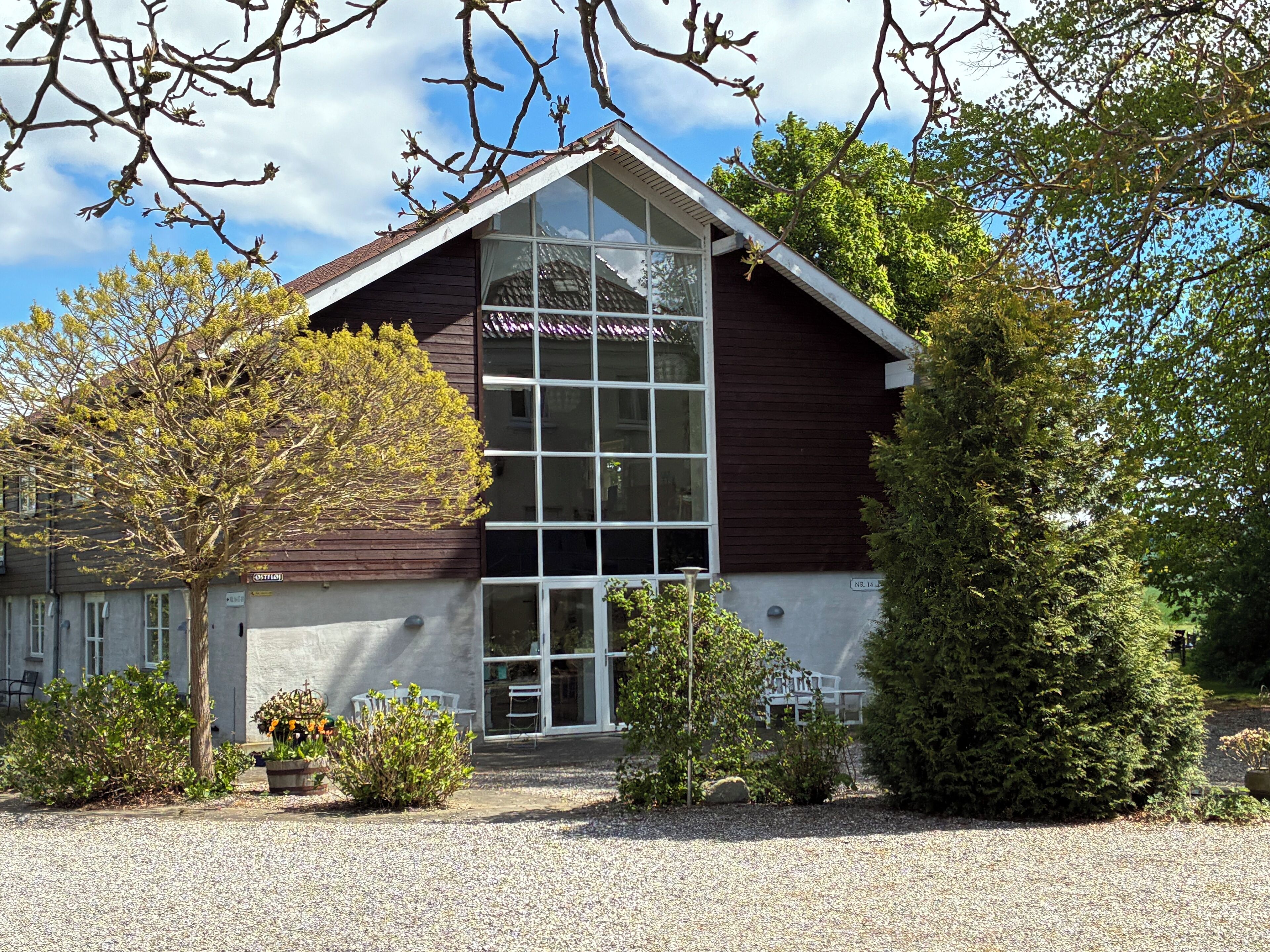 A building with a large window, a sloped roof, and a gravel driveway.