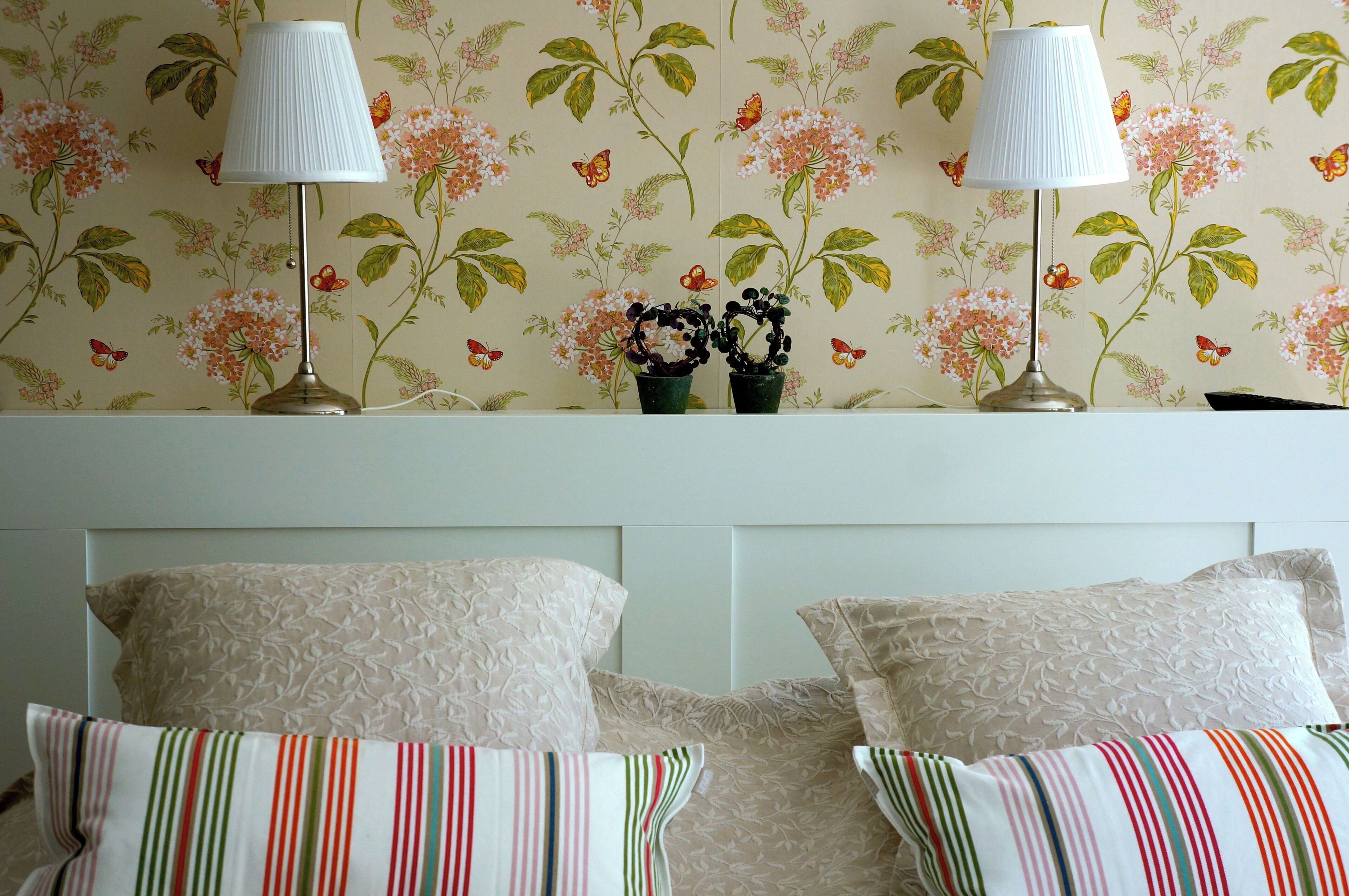 A bedroom with floral wallpaper, two lamps, and striped pillows.