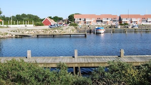 Un port de plaisance au bord de l’eau, avec des bateaux amarrés, un bâtiment rouge et une rangée de maisons aux toits rouges.